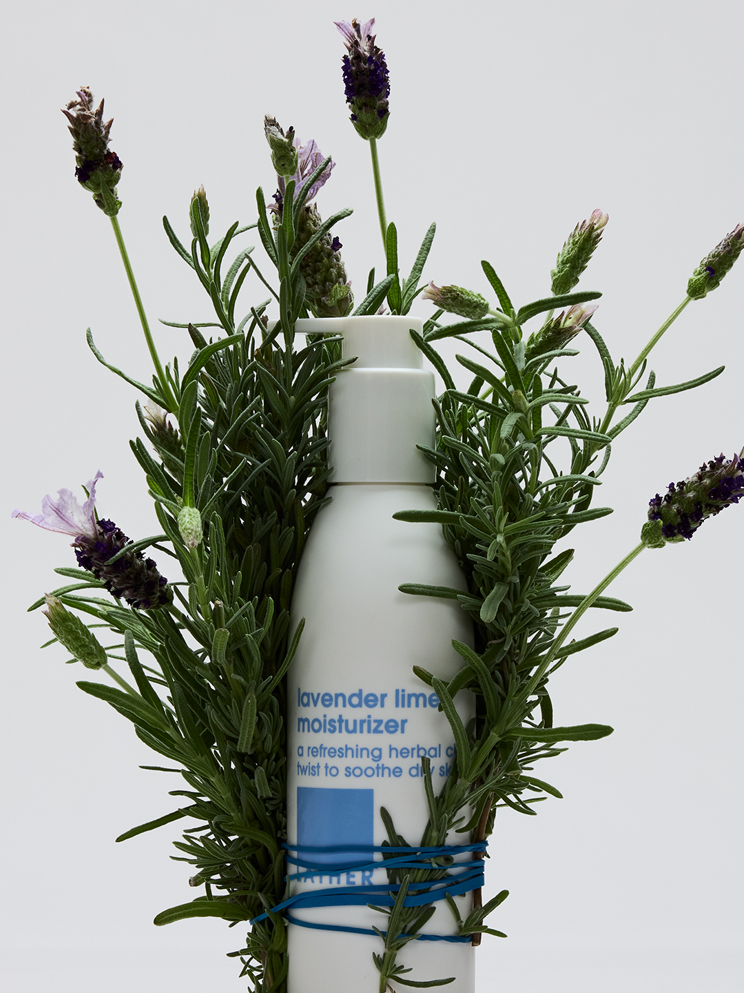 A bottle of Lather lavender lime moisturizer nestled in a bundle of fresh lavender and rosemary sprigs.
