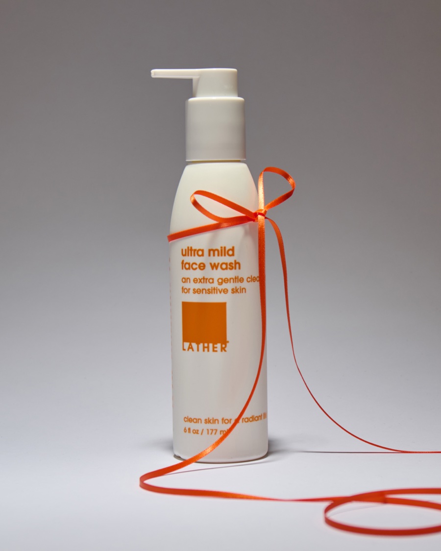 A bottle of Lather ultra mild face wash tied with a thin orange ribbon that trails across a soft grey backdrop.
