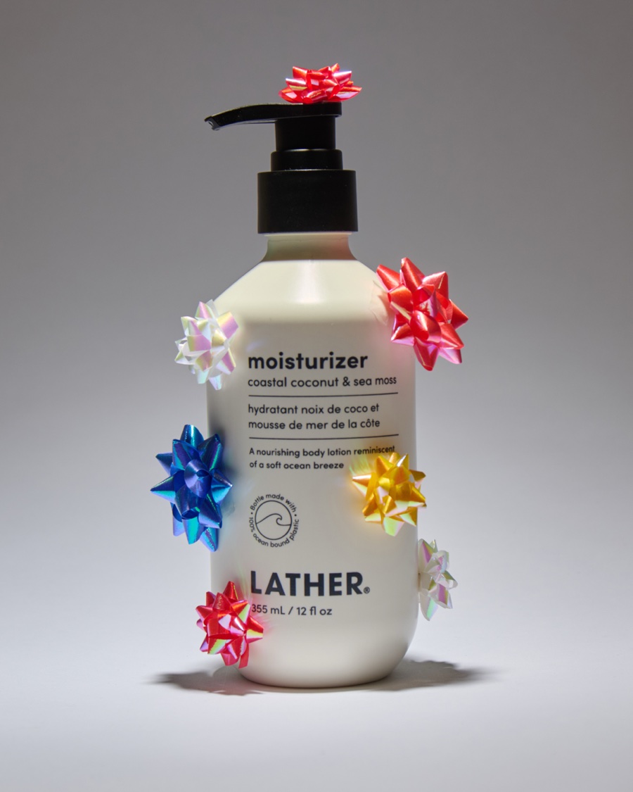 A bottle of Lather coastal coconut & sea moss moisturizer dotted with iridescent gift bows in pink, blue, and gold.