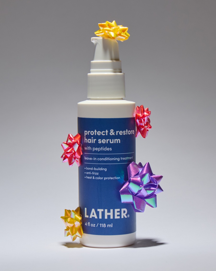 A bottle of Lather protect & restore hair serum covered in shiny gift bows in gold, pink, and purple.