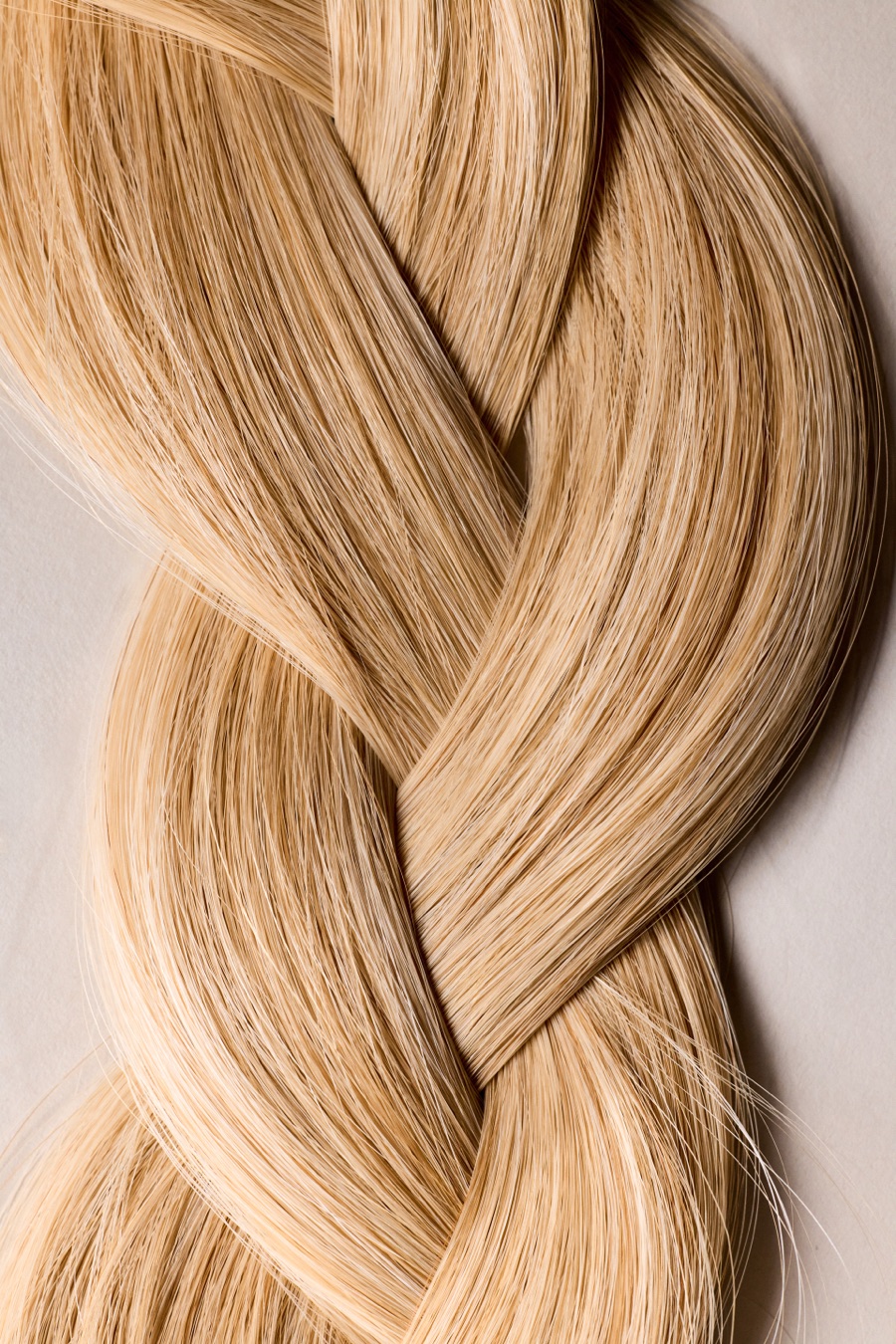 Close-up of a thick, glossy honey-blonde braid against a pale backdrop.