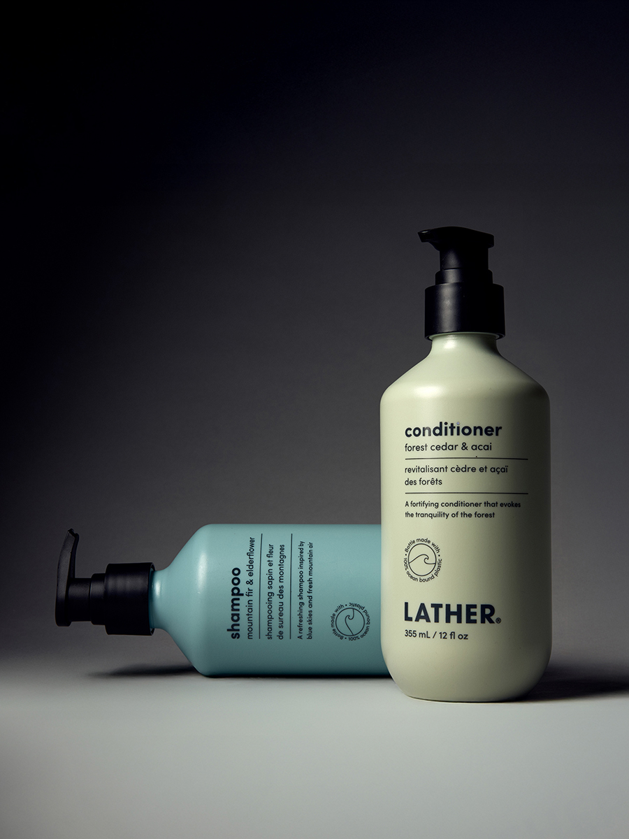 Lather mountain fir & elderflower shampoo and forest cedar & acai conditioner bottles standing together against a dark gradient background.