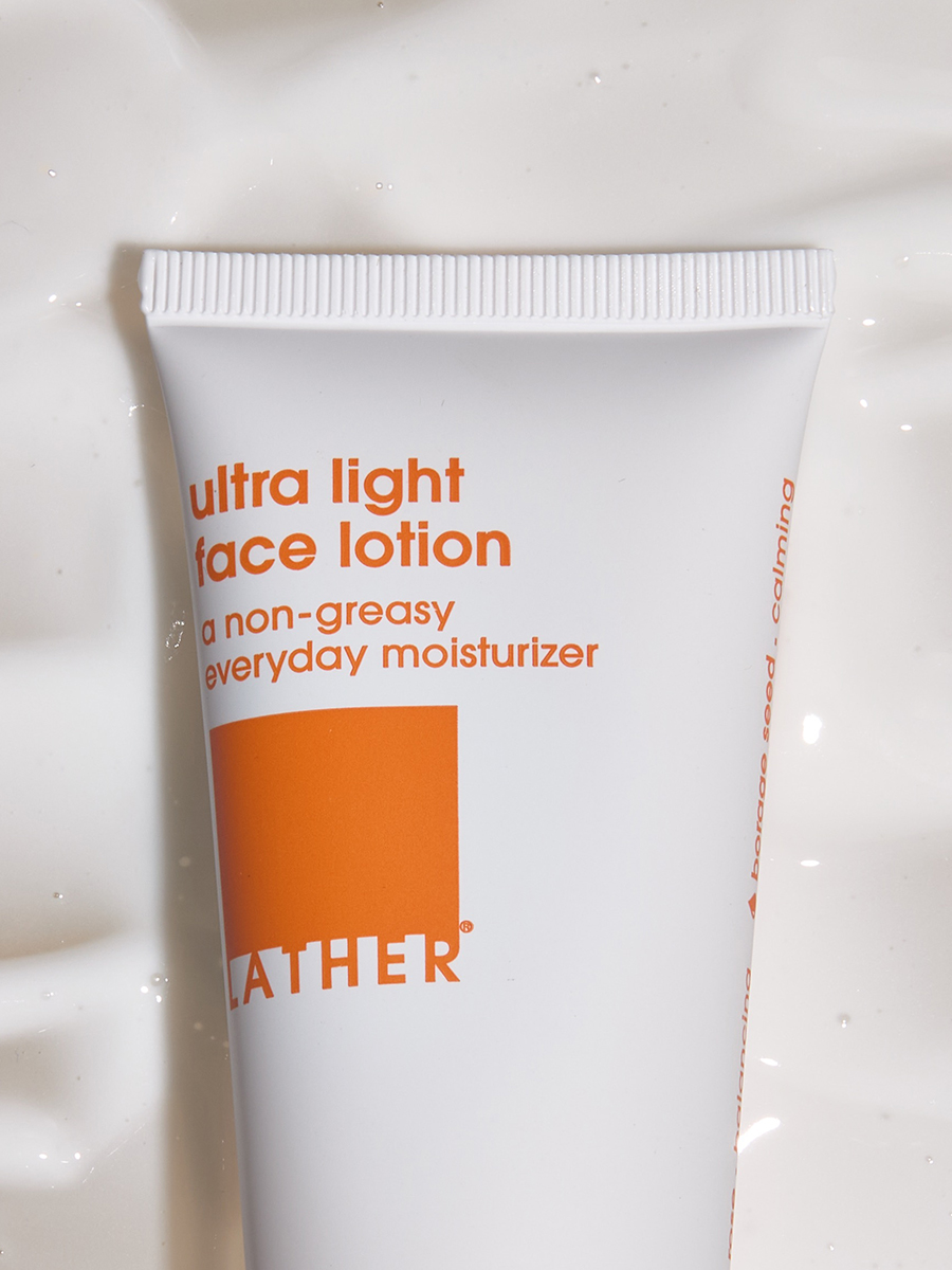 A tube of Lather ultra light face lotion lying on a rippled, wet white surface.