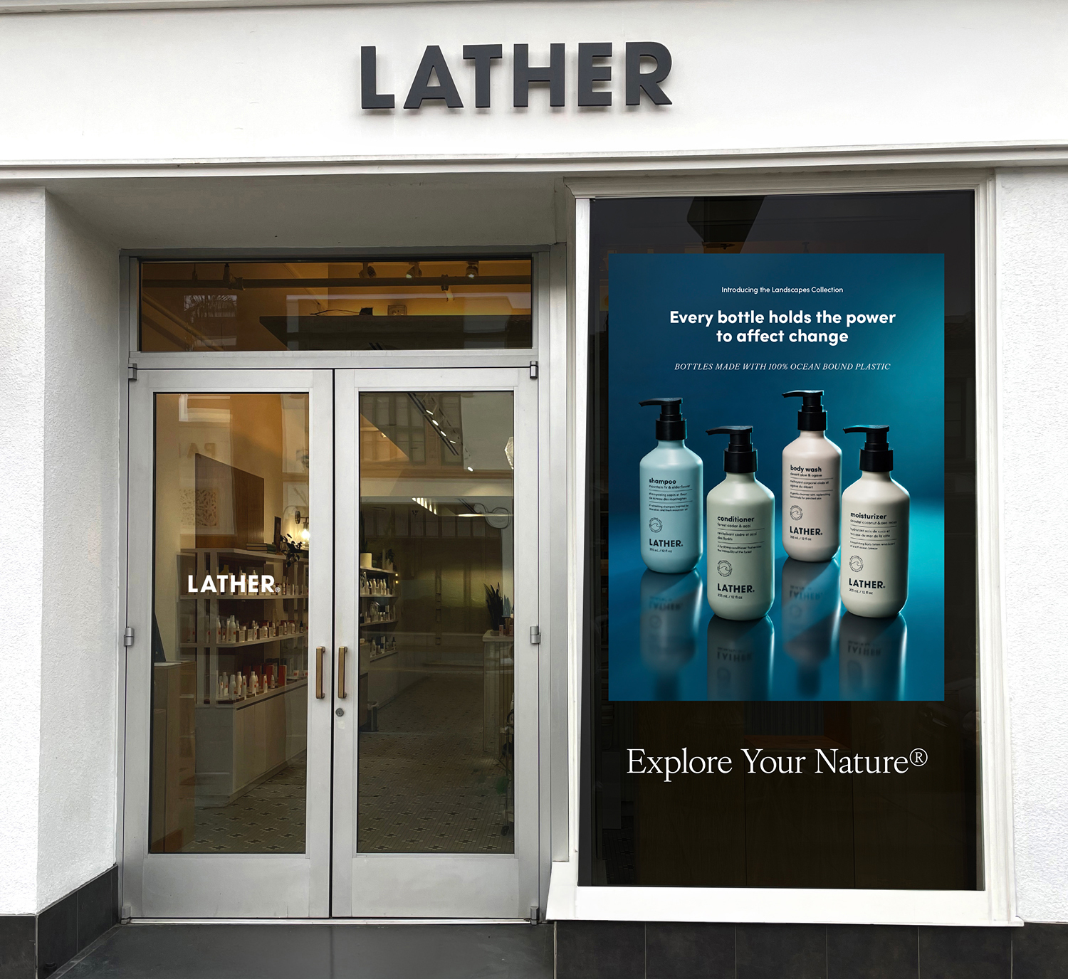 LATHER storefront with a store window decal introducing the Landscapes Collection — the shampoo, conditioner, body wash, and moisturizer bottles over a teal gradient, reading 'Every bottle holds the power to affect change' and 'Explore Your Nature.'
