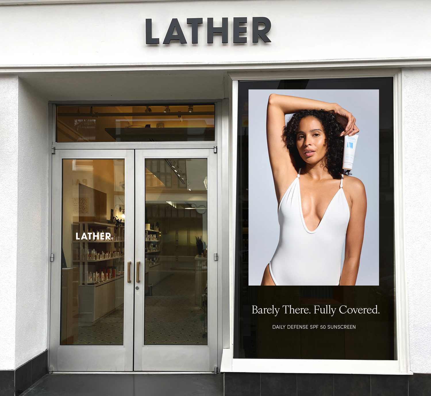 LATHER storefront with a store window decal reading 'Barely There. Fully Covered. Daily Defense SPF 50 Sunscreen,' featuring a model holding the product tube above her shoulder.