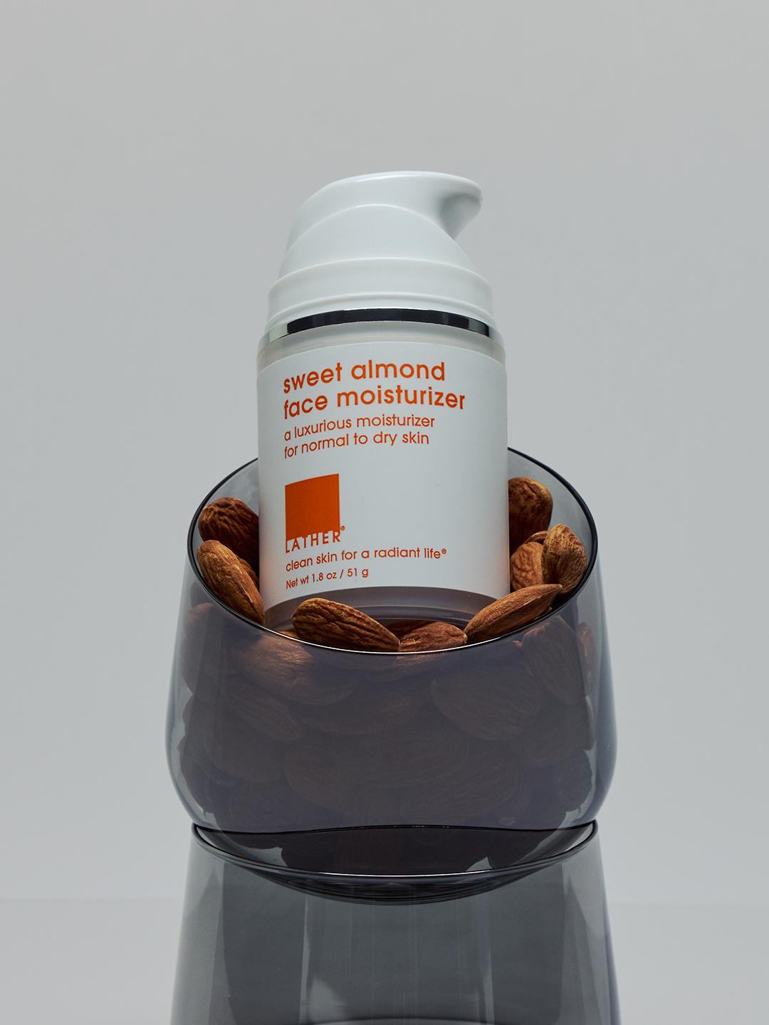 Lather Sweet Almond Face Moisturizer standing in a glass bowl filled with whole almonds.