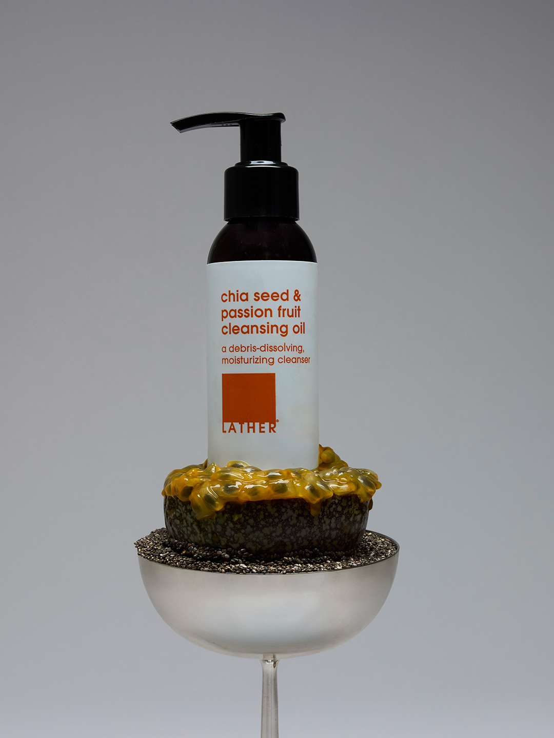 Lather Chia Seed & Passion Fruit Cleansing Oil with passion fruit pulp draped over its cap, set on a bed of chia seeds in a coupe glass.