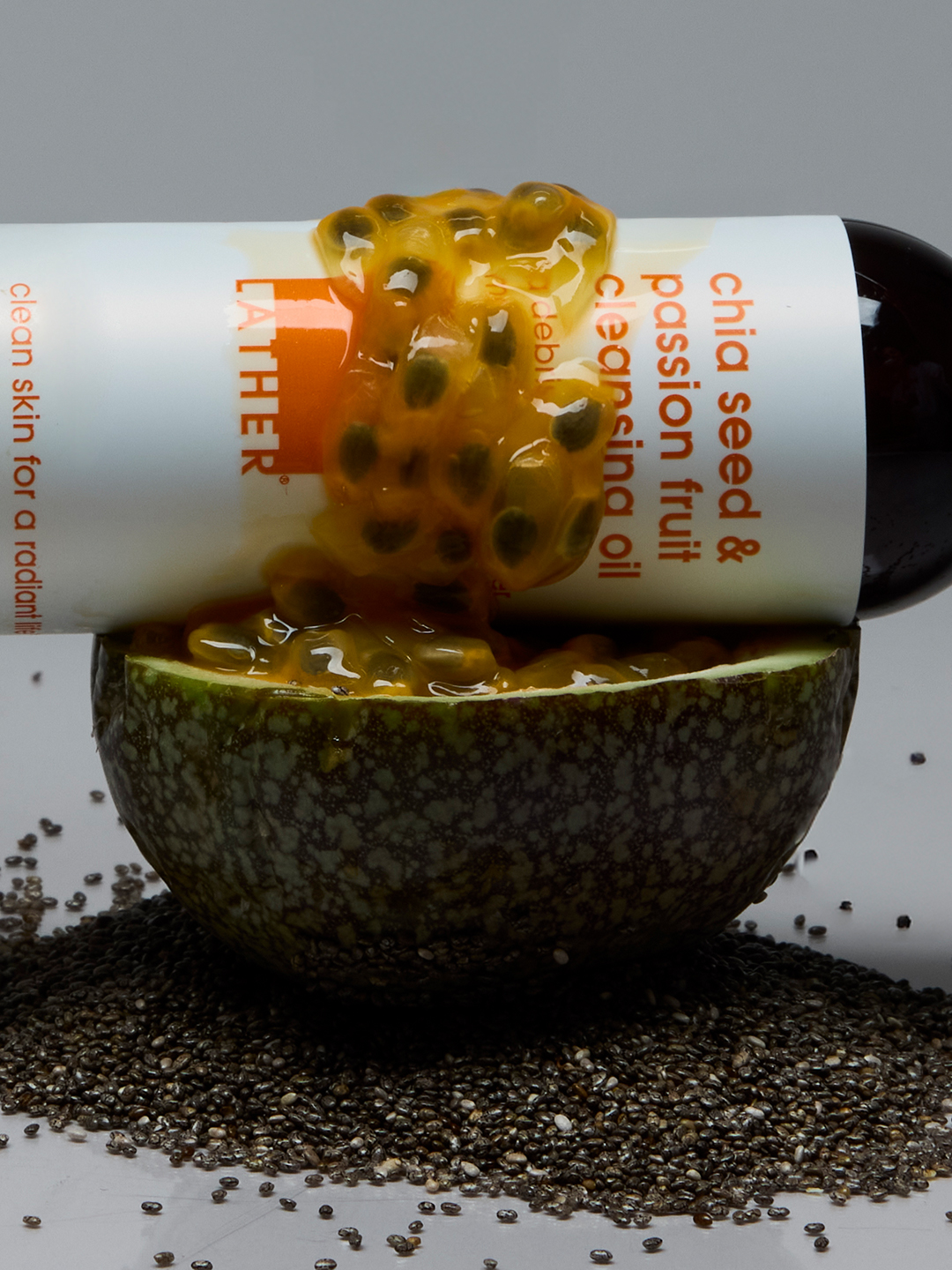 Lather Chia Seed & Passion Fruit Cleansing Oil lying on its side beside a halved passion fruit, chia seeds scattered across the surface.