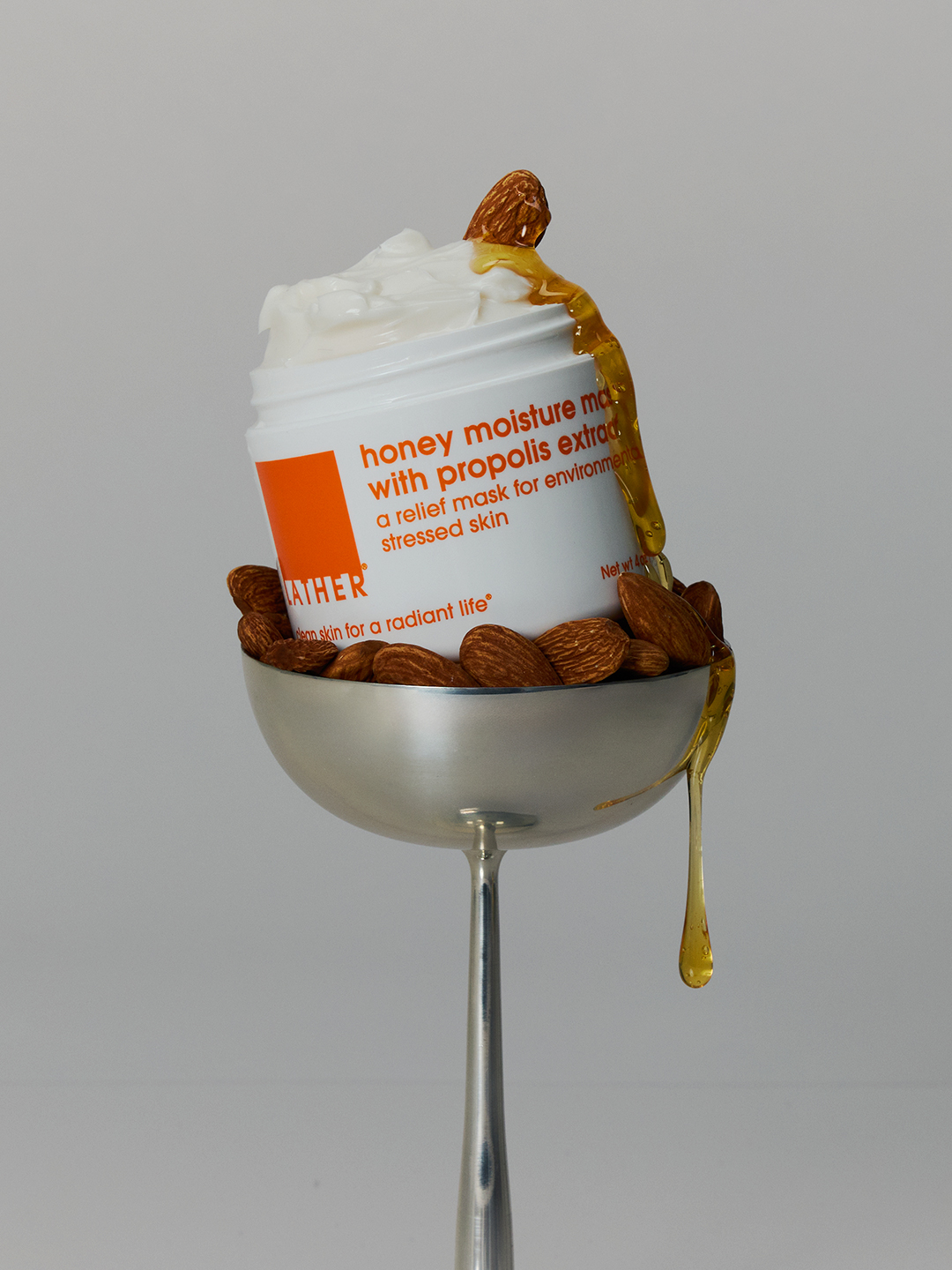 Lather Honey Moisture Mask with Propolis Extract resting in a silver coupe bowl of almonds, honey dripping down the jar.