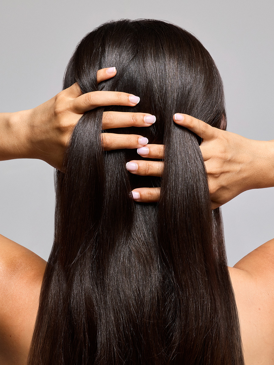 A bottle of LATHER Protect & Restore Hair Serum standing in front of a long, glossy sheet of straight auburn hair.